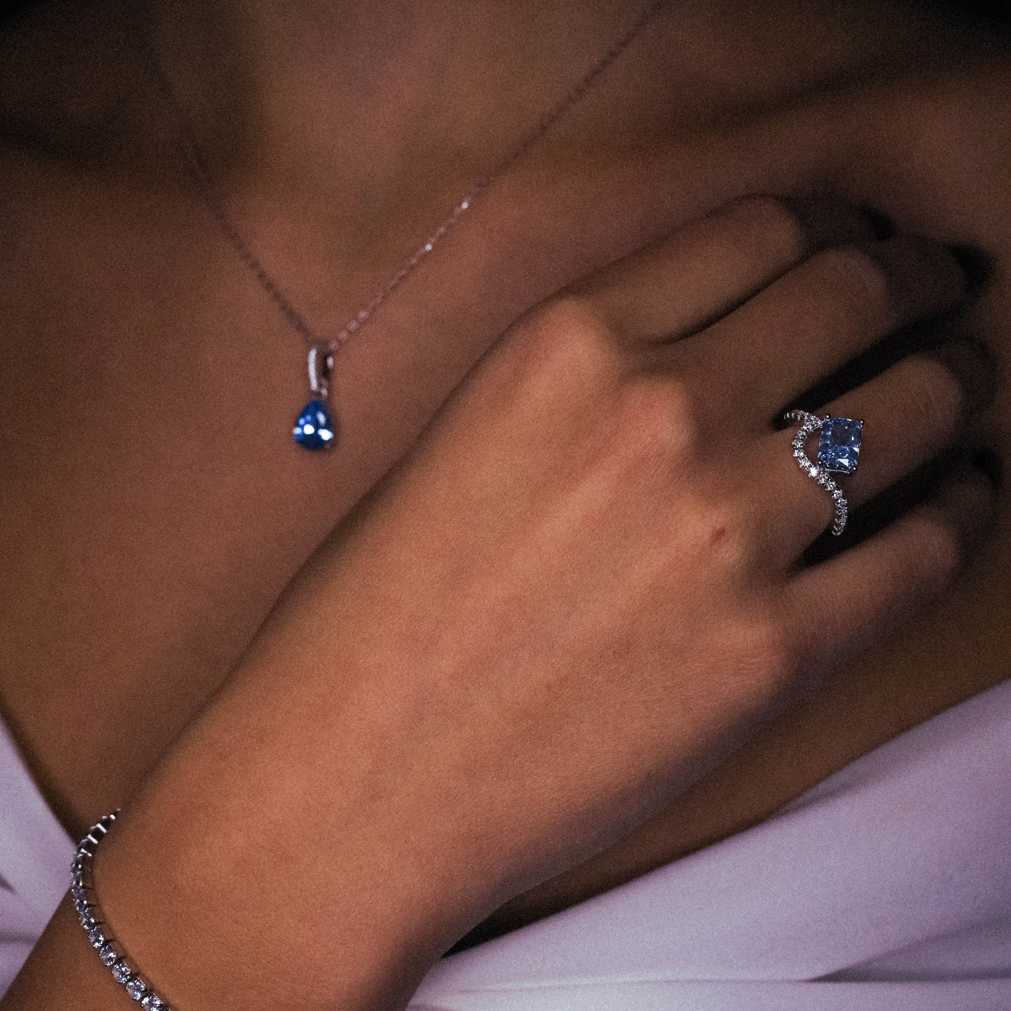 Close-up of the Ring Blue Water, showcasing the sharp rectangular cut of the rich blue gemstone. The sleek, polished sterling silver band curves gently, accentuating the stone's brilliance with its smooth and modern finish. Worn on the hand, combined with the lost princess necklace in blue, as well as the silver, adjustable tennis bracelet