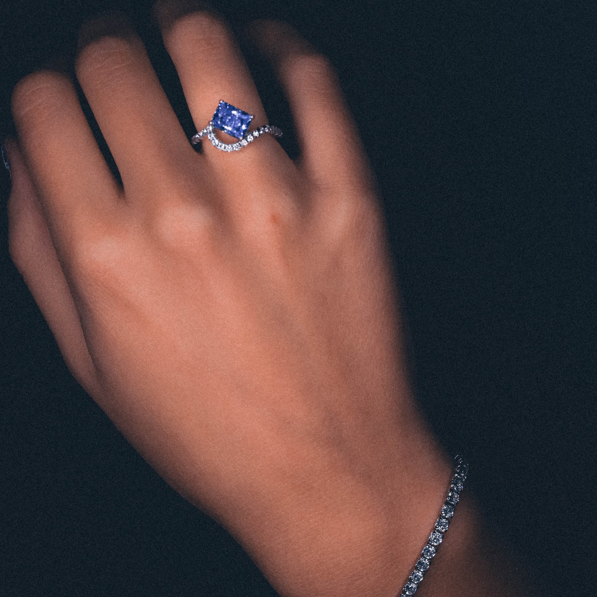 Close-up of the Ring Blue Water, showcasing the sharp rectangular cut of the rich blue gemstone. The sleek, polished sterling silver band curves gently, accentuating the stone's brilliance with its smooth and modern finish. Worn om the hand, combined with our silver and adjustable, classic tennis bracelet.