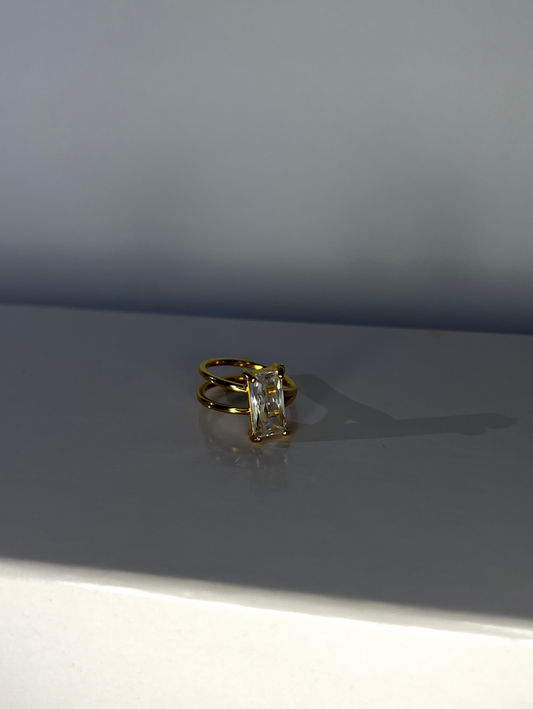 elegant ring featuring a large rectangular white cubic zirconia stone set on an asymmetrical bangle, made of 18K gold-plated stainless steel.